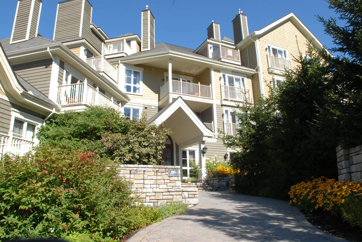 Exterior view of a multi-story condo building with balconies, stone accents, and lush landscaping.