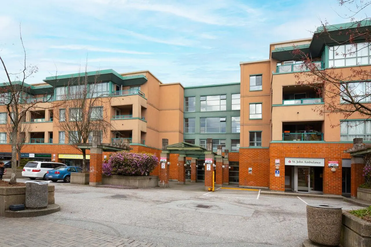 Exterior of a multi-story building with tan and green accents, brick base, and St. John Ambulance signage. Cars parked nearby.
