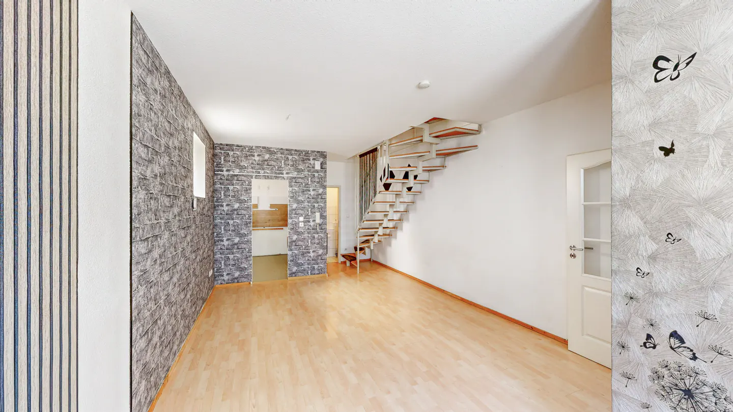An interior shot of a room with hardwood floors, a staircase, and patterned wallpaper.