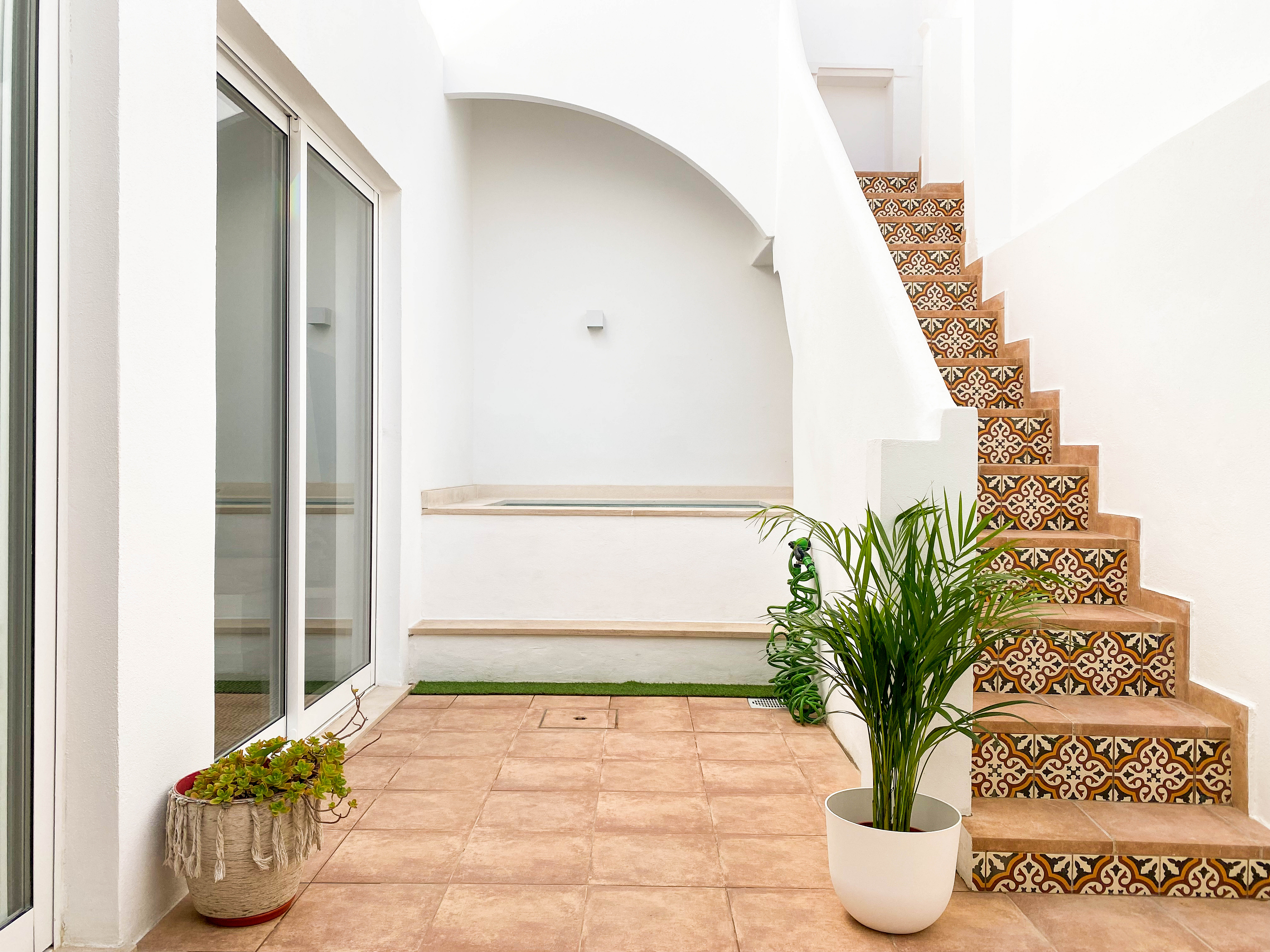 A bright patio with terracotta tiles, a small plunge pool, and a staircase featuring decorative patterned tiles. [AI-generated text]
