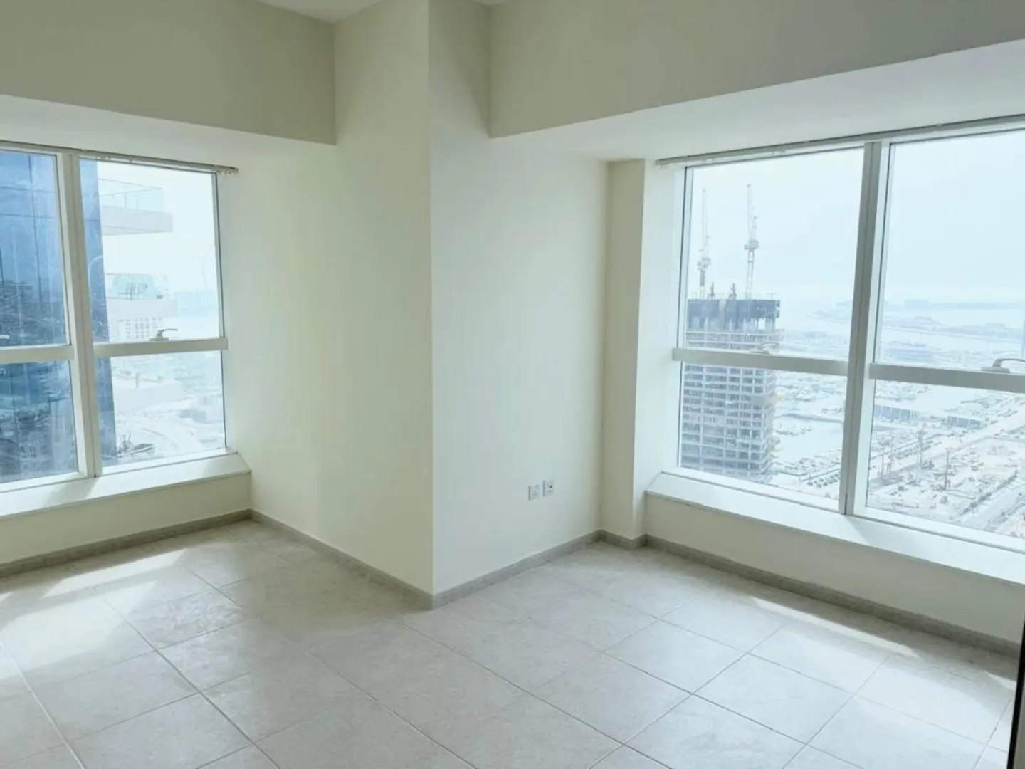 Empty room with tile floor, white walls, and two large windows with city views.