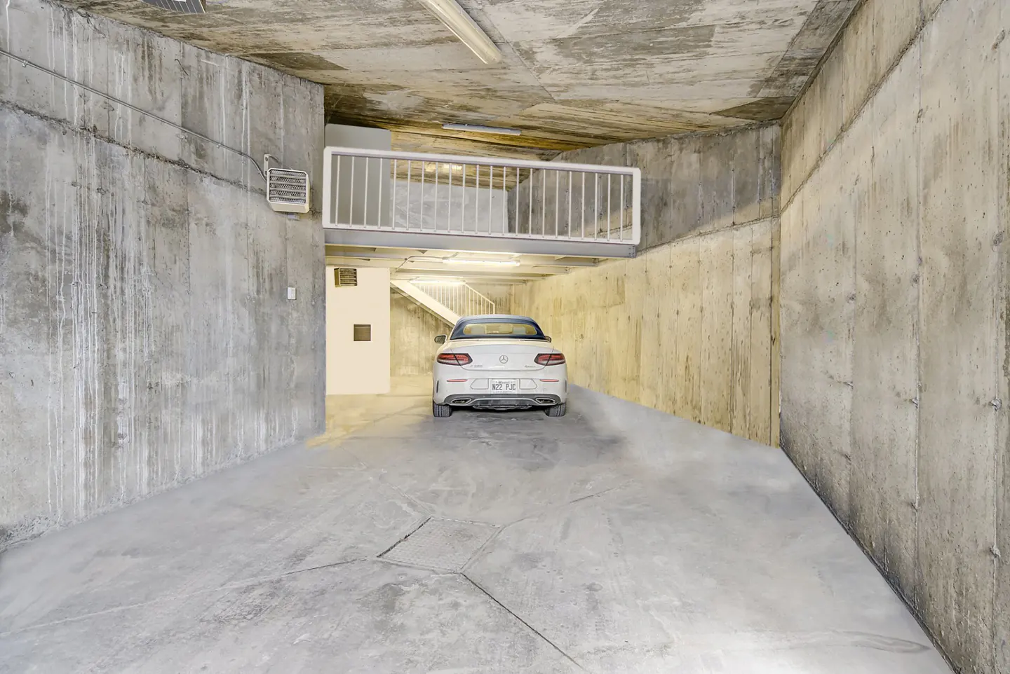 Concrete garage interior with a white car parked inside. A white staircase is visible in the background.