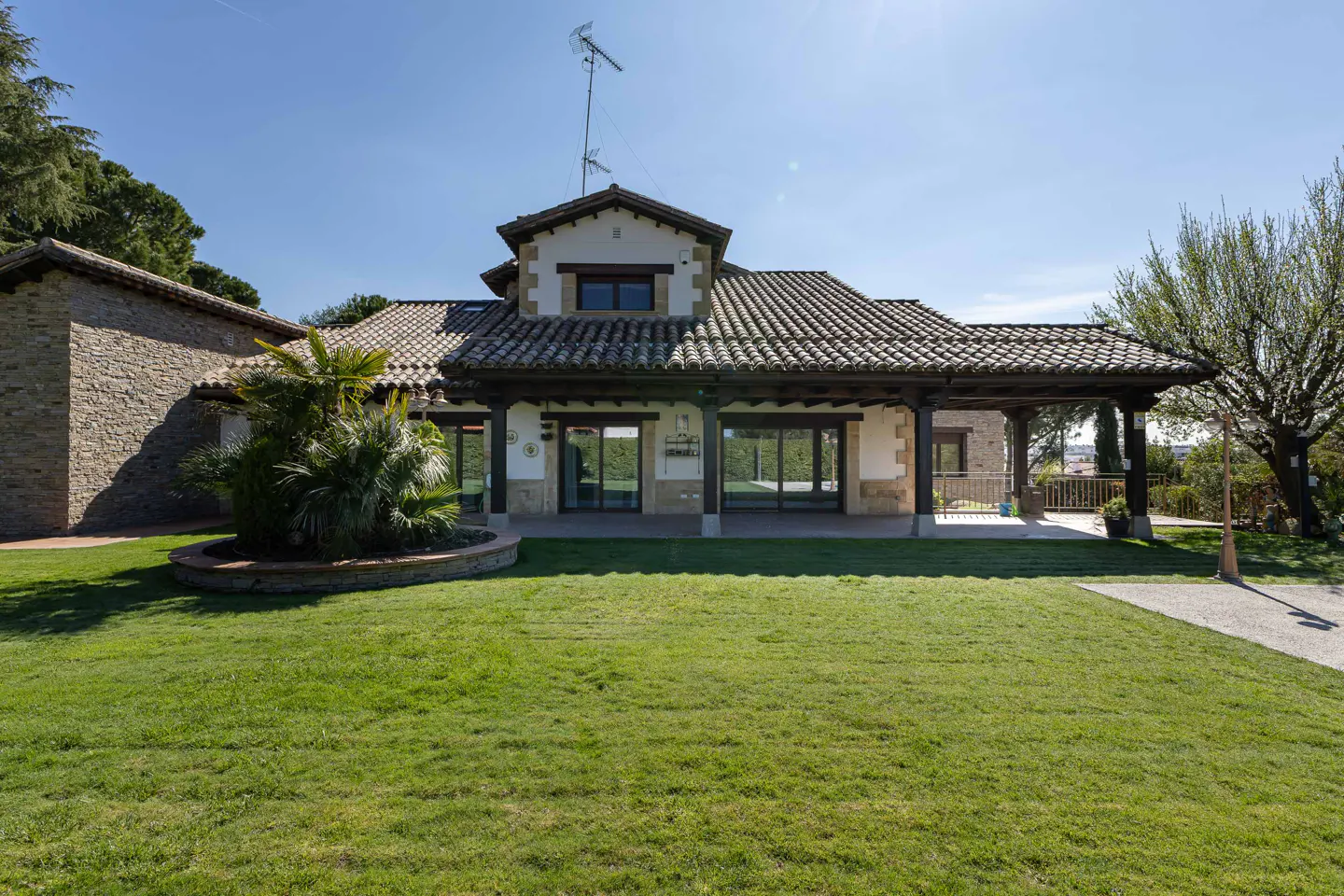 Exterior view of a stone house with a tiled roof and a green lawn on a sunny day.