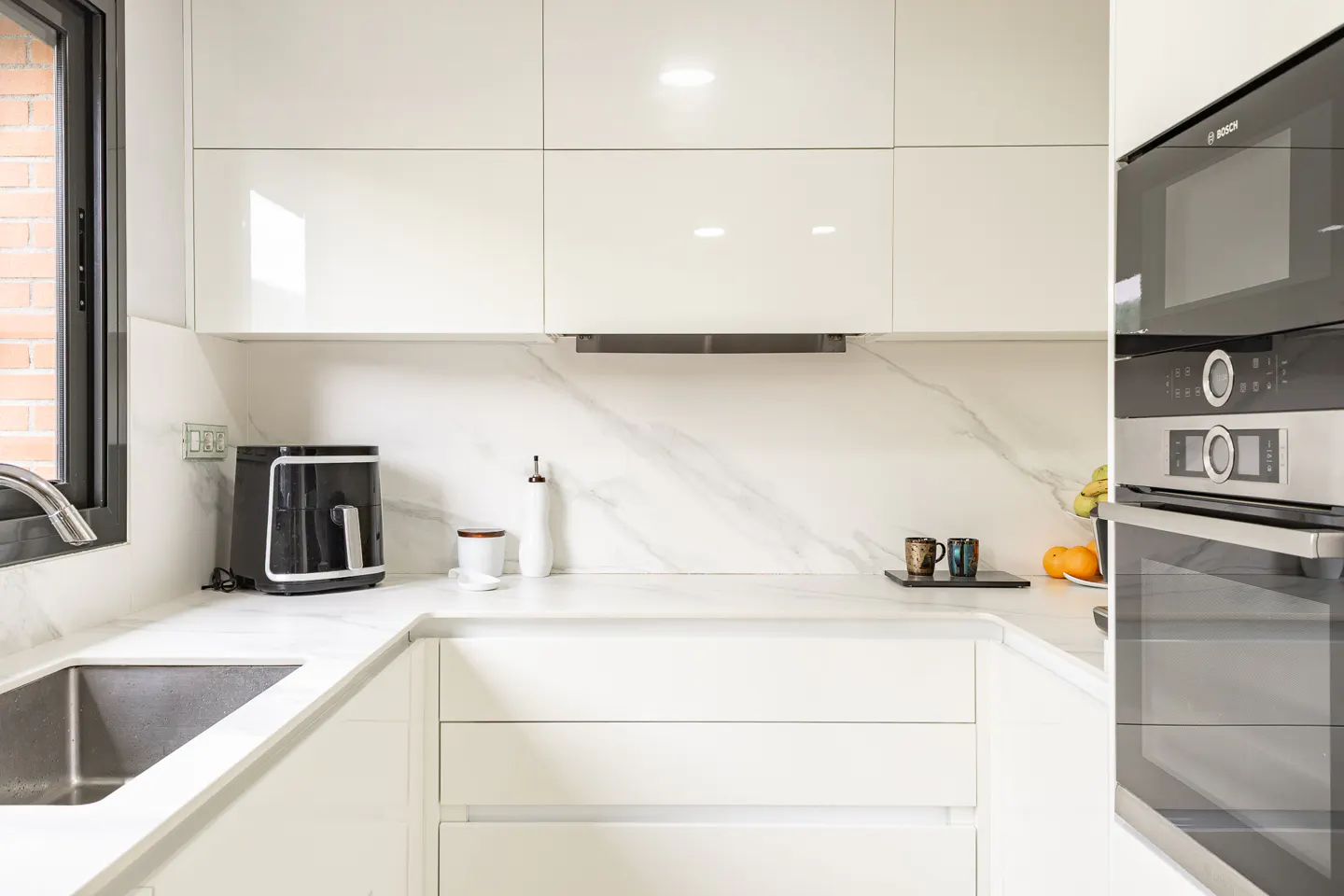 Bright, modern kitchen with white cabinets, marble countertops, and stainless steel appliances. A black air fryer sits near the sink.