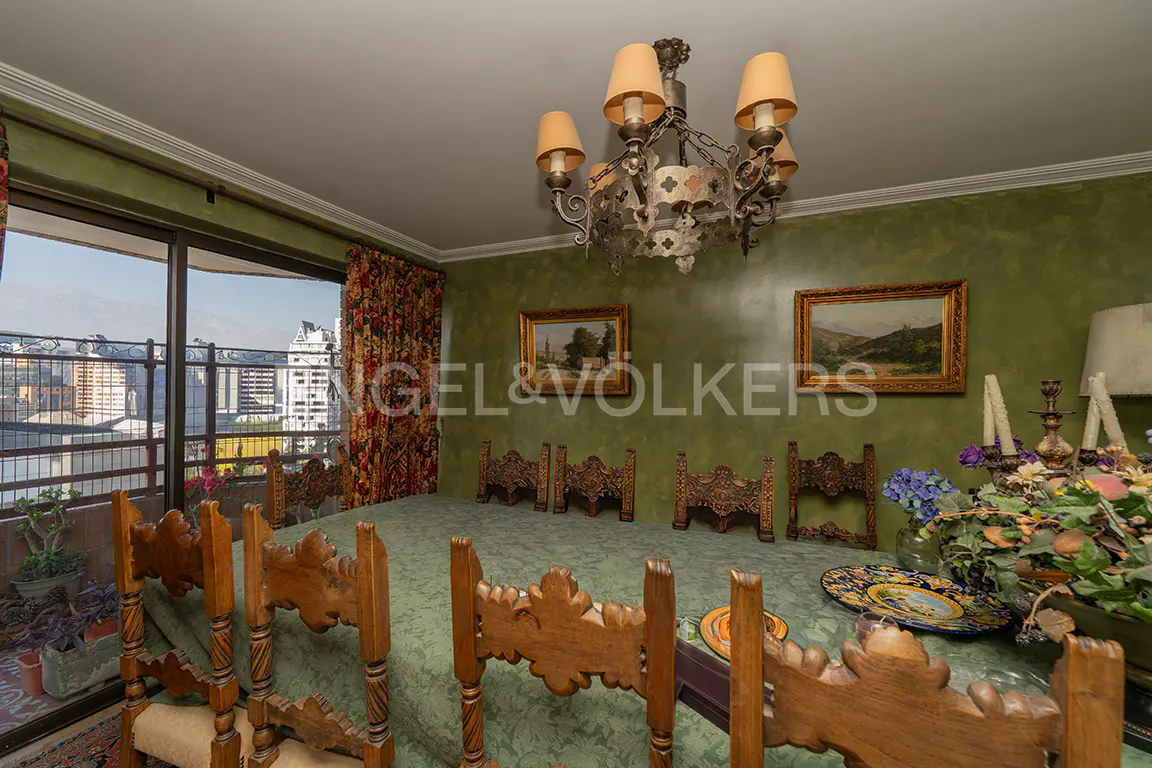 Dining room with green walls, a large wooden table, and a chandelier. Balcony with city view. Engel & Volkers logo on the wall.