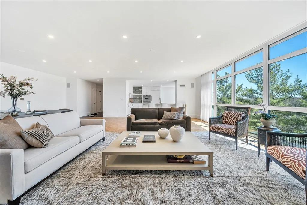 Bright, modern living room with white sofa, brown sofa, zebra print chairs, and large windows with a view of trees.