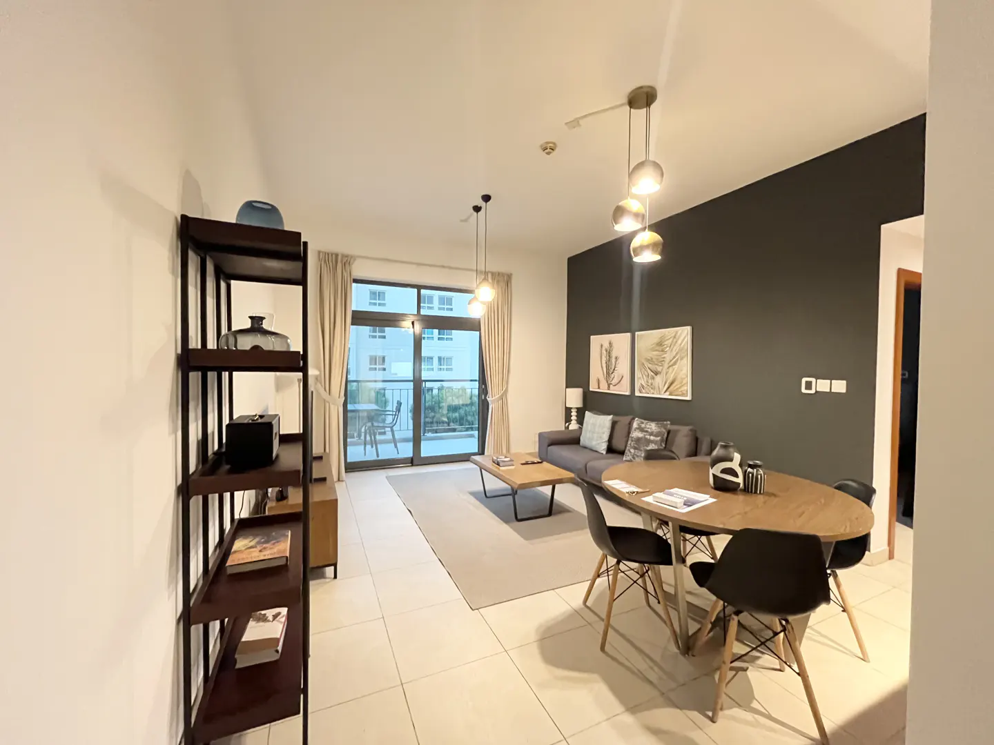 A modern apartment living room with a dining table, gray sofa, and a balcony with a view.