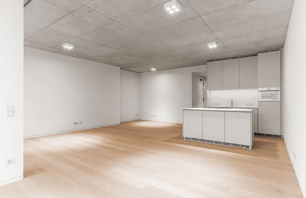 Minimalist kitchen with white cabinets, island, and light wood floors. Concrete ceiling with recessed lighting.