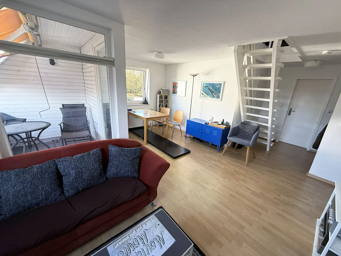 A bright living room with a red sofa, wooden floors, and a white staircase leading to an upper level.