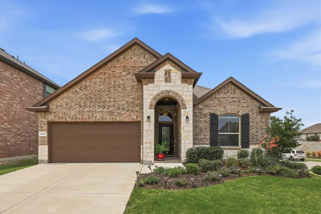 A single-story brick house with a brown garage door, stone archway, and manicured lawn under a blue sky.