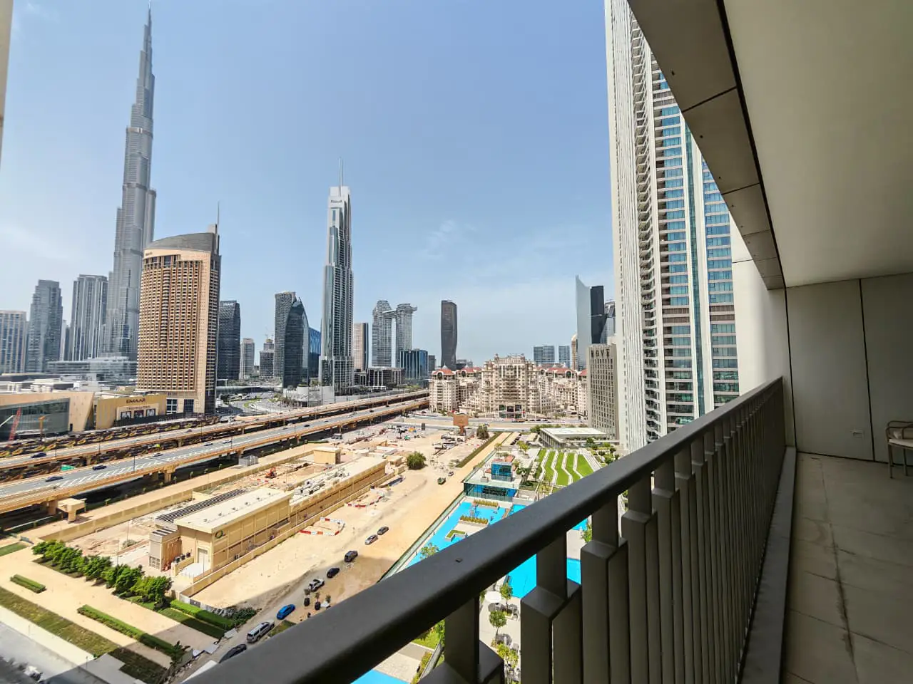 View from a balcony overlooking the Dubai skyline, including the Burj Khalifa, with a pool and buildings below.