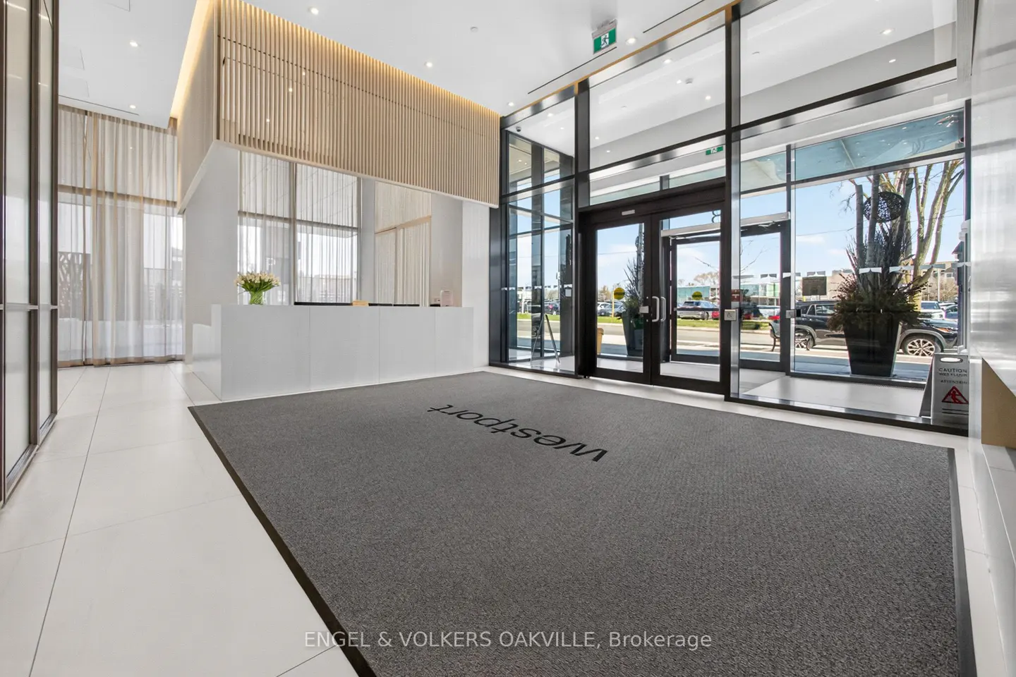 Modern lobby with white reception desk, wood accent wall, and glass doors leading outside. Gray carpet with "Westport" logo.