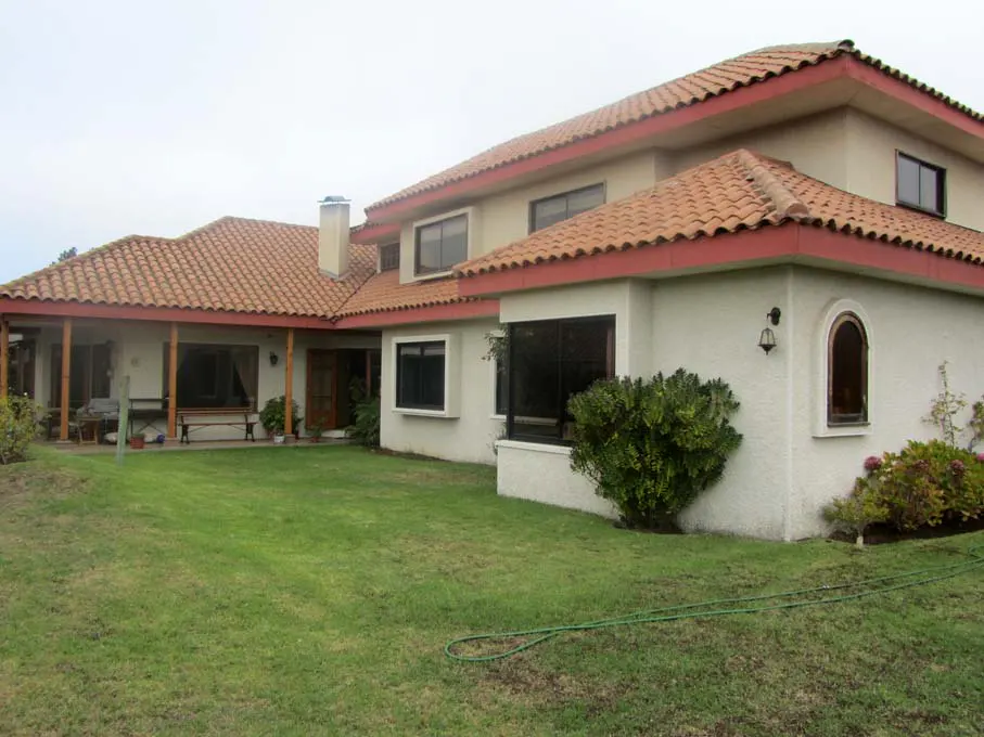Two-story house with a red tile roof and a green lawn. The house has white walls and black-framed windows. A green hose is on the lawn.