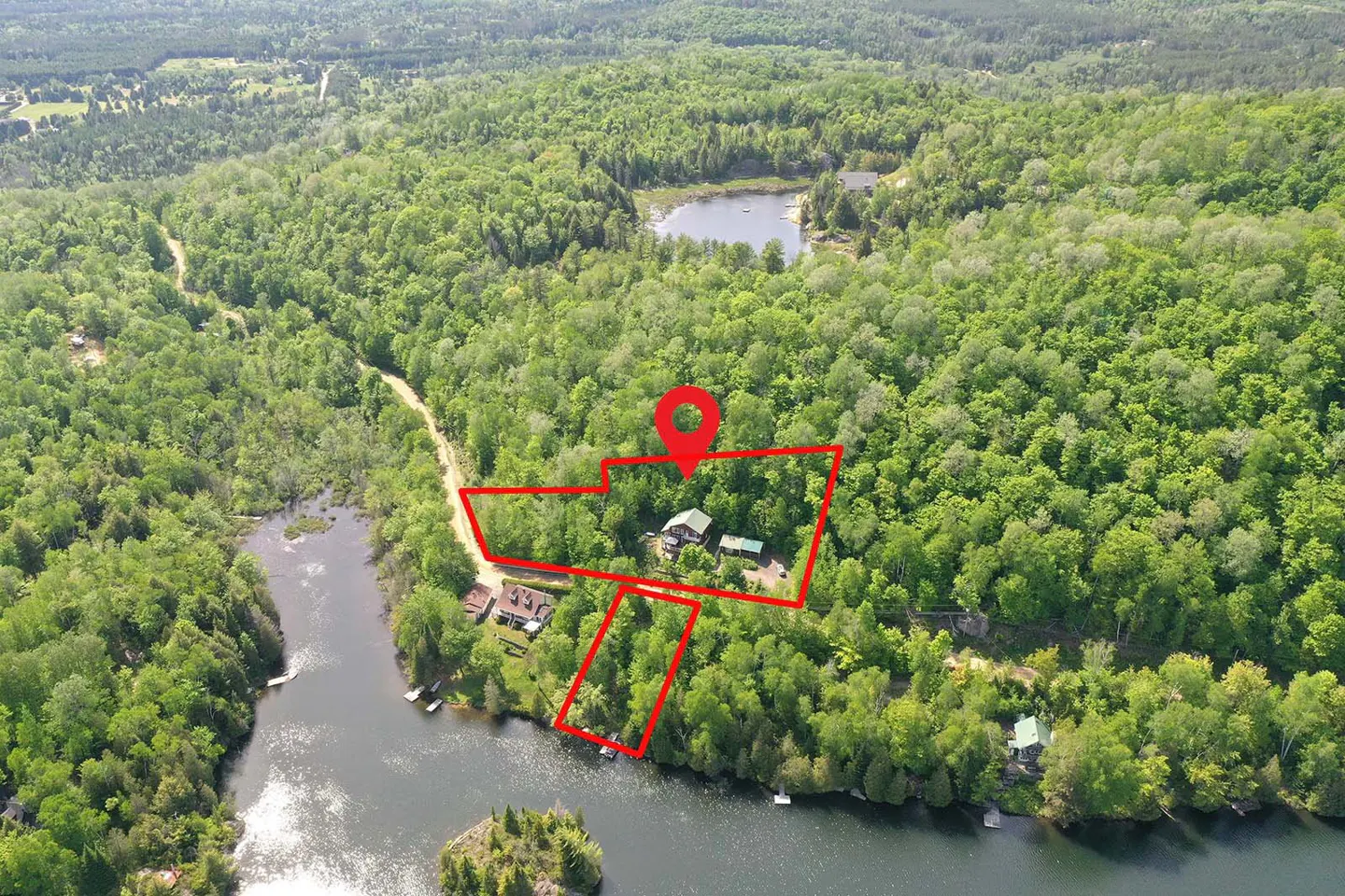 Aerial view of a wooded property outlined in red, featuring a house near a lake with a red location pin above.