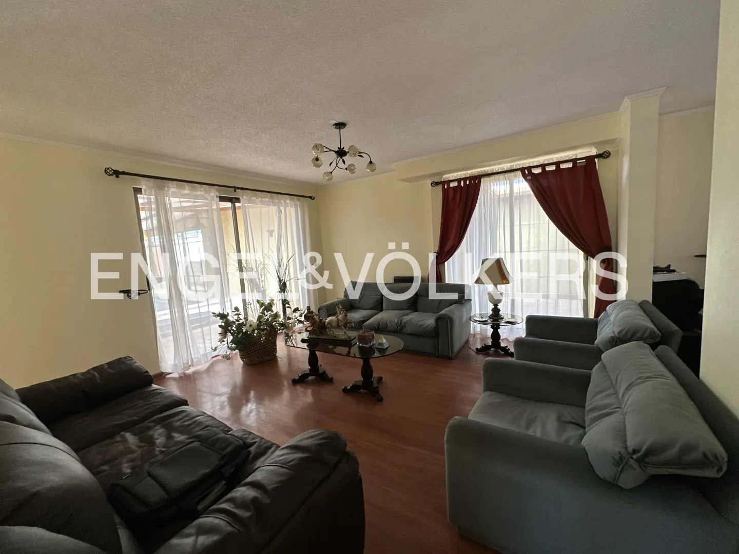 A living room with wood floors, sofas, chairs, tables, and curtains. The walls are light yellow. There is a chandelier on the ceiling.