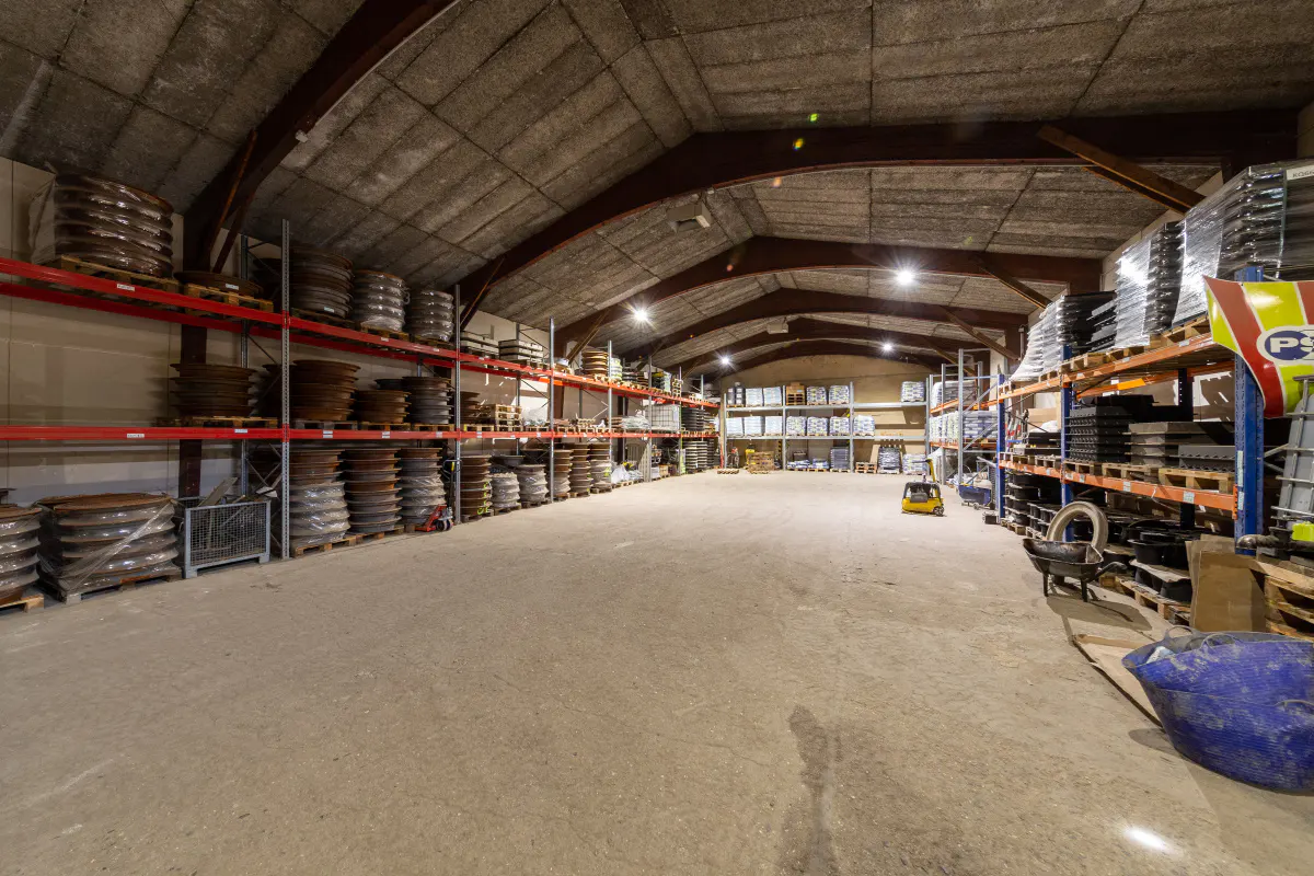 A large warehouse with high ceilings and rows of shelves stocked with goods. A forklift is visible in the distance.