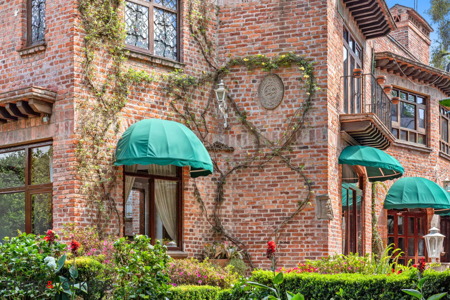 Exterior of a red brick building with green awnings, vines, and manicured hedges.