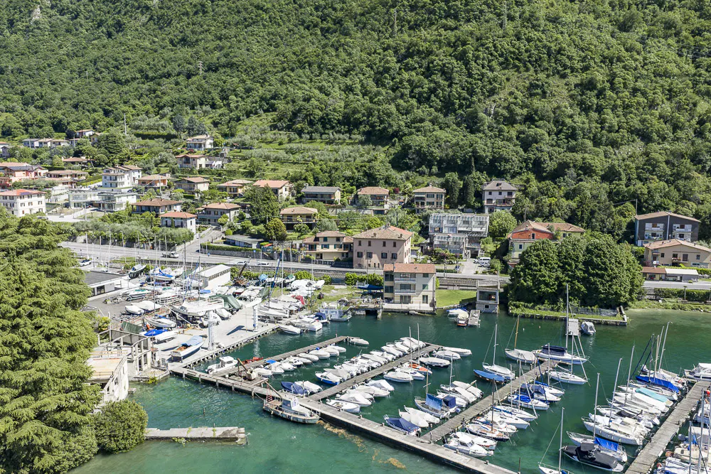 Aerial view of a marina with many boats docked in turquoise water, a town, and a green forested hillside.