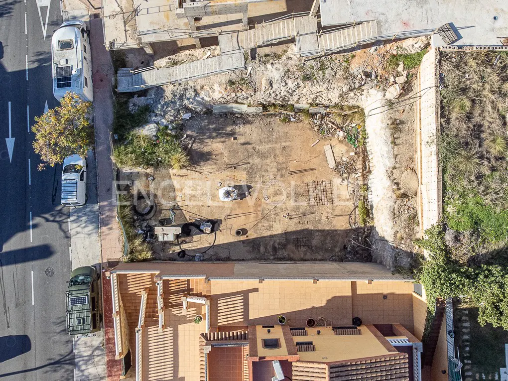 Aerial view of a vacant lot with construction debris, bordered by a street with parked vehicles and adjacent buildings.