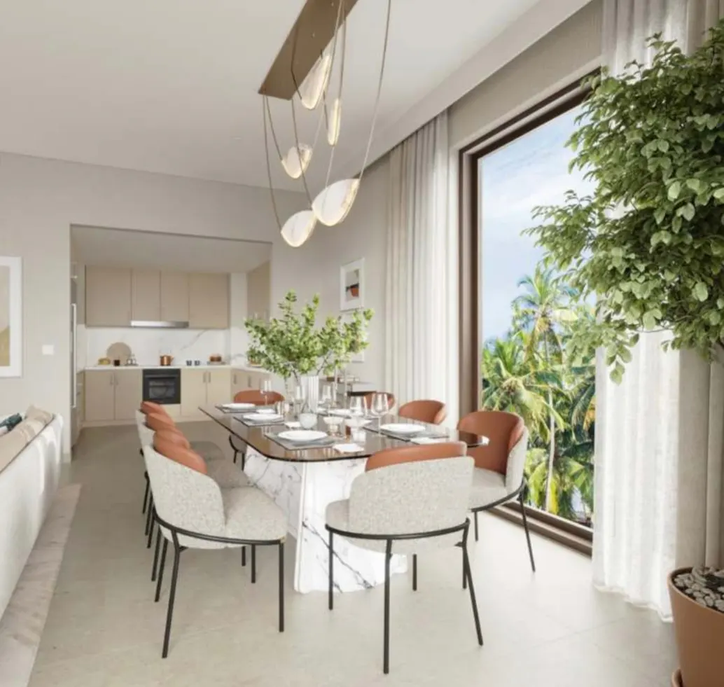 Bright, modern dining area with a marble table, upholstered chairs, and a view of palm trees through a large window. A modern chandelier hangs above.