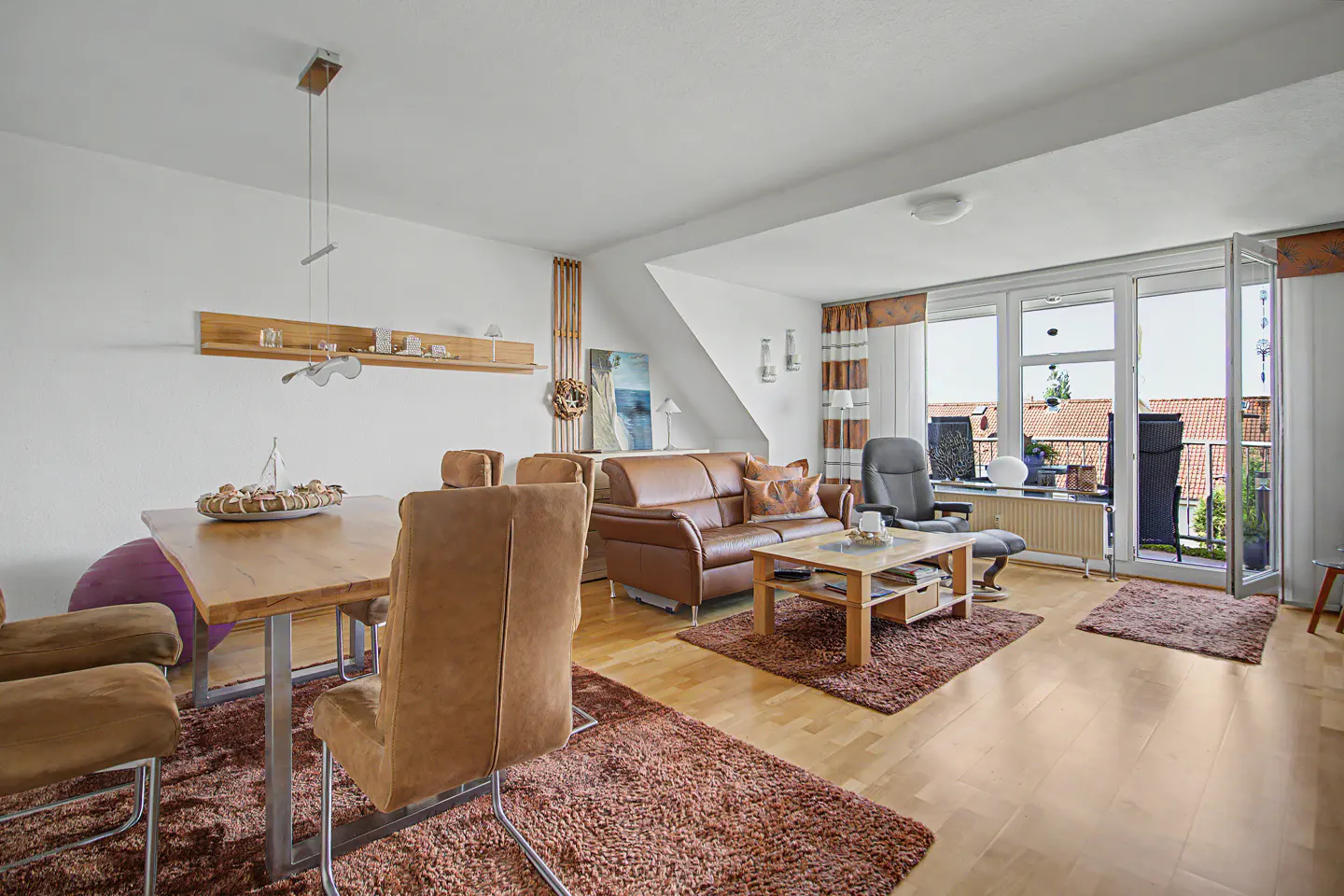 Bright living and dining room with light wood floors, brown leather sofa, dining set, and balcony access.