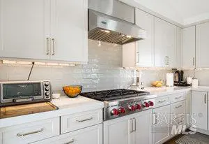 Bright kitchen with white cabinets, stainless steel range hood, and gas cooktop. A toaster oven sits on the counter.