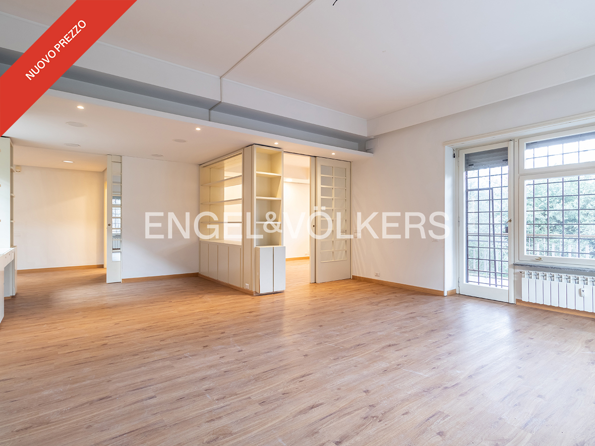 Bright, empty living room with light wood floors, white walls, built-in shelving, and a glass door leading to a balcony.