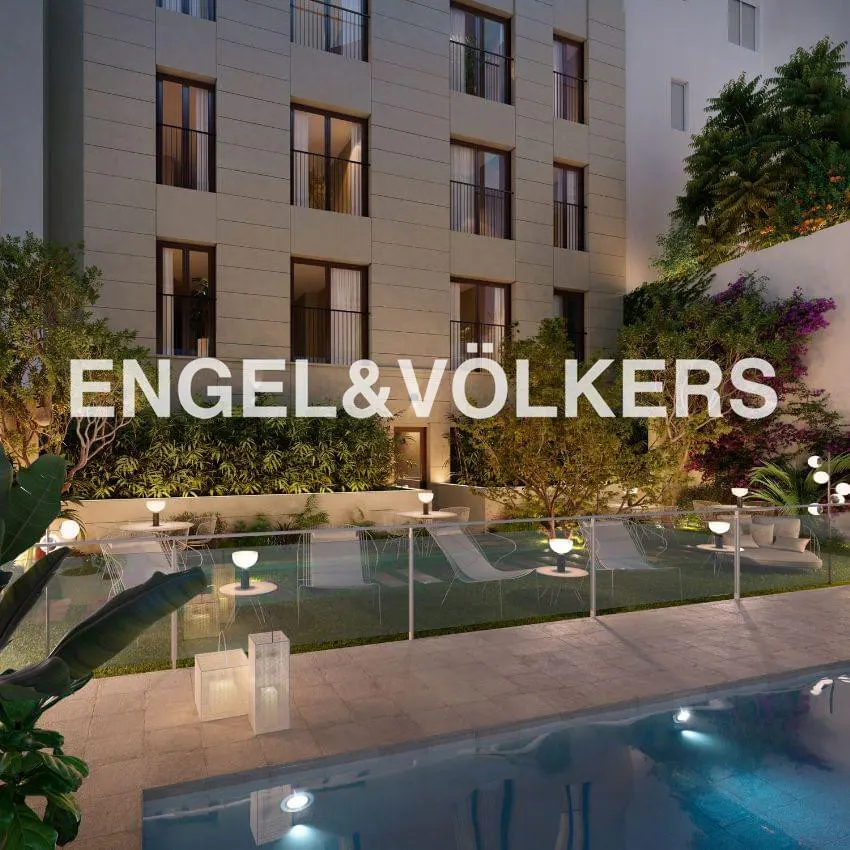 Exterior view of a modern apartment building with a pool, lounge chairs, and the Engel & Völkers logo.