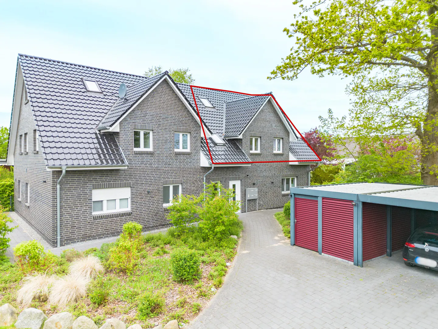 Two-story gray brick house with a dark gray roof, white trim, and a red-doored garage with a car parked inside.