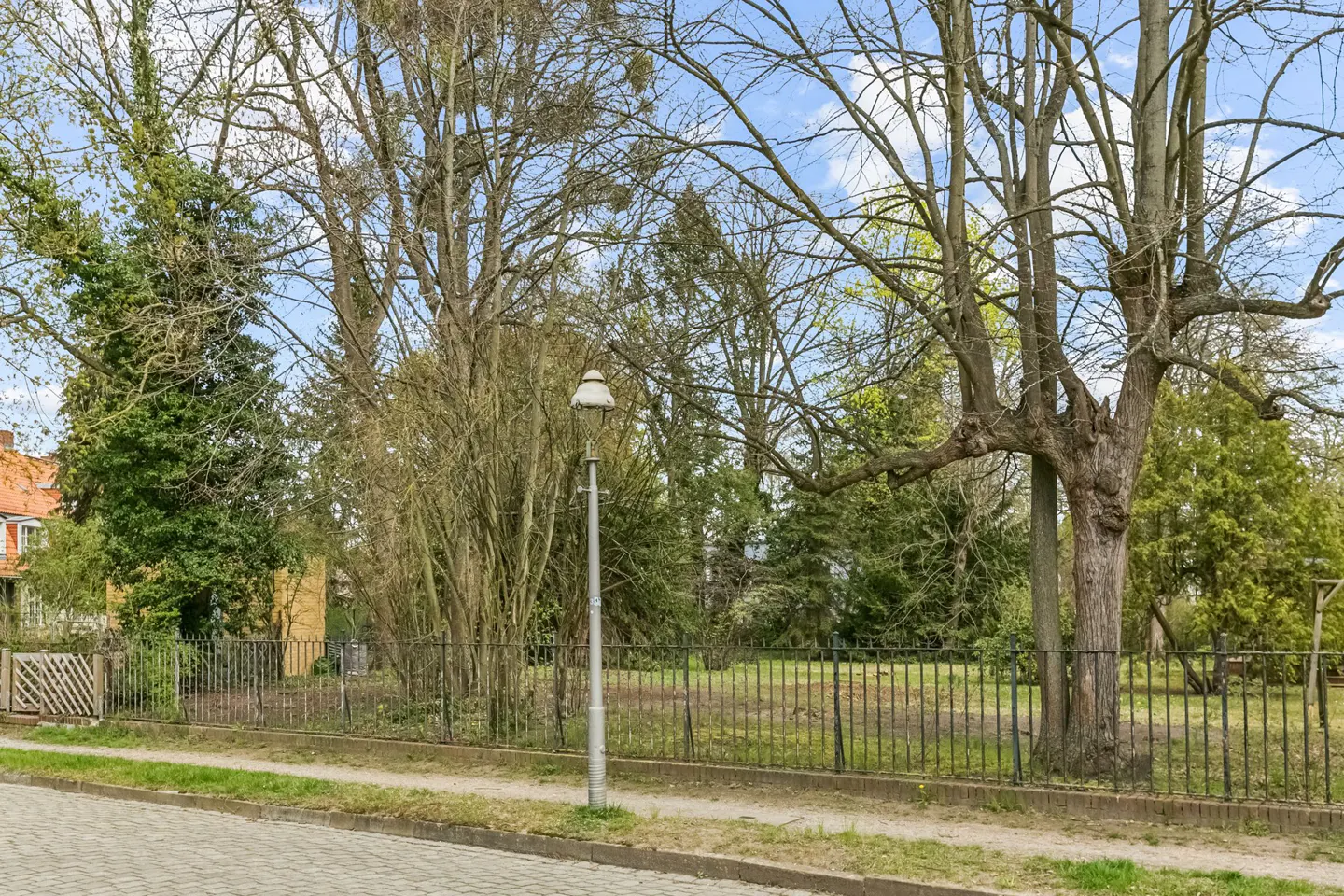 A street view of a property with a black metal fence, trees, and a lamp post.