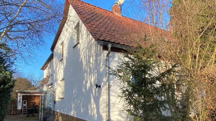 Exterior view of a two-story white house with a red tile roof, surrounded by trees under a blue sky.