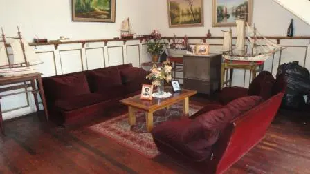 Living room with hardwood floors, burgundy sofa and chair, wood coffee table with flowers, and model ships on a shelf.