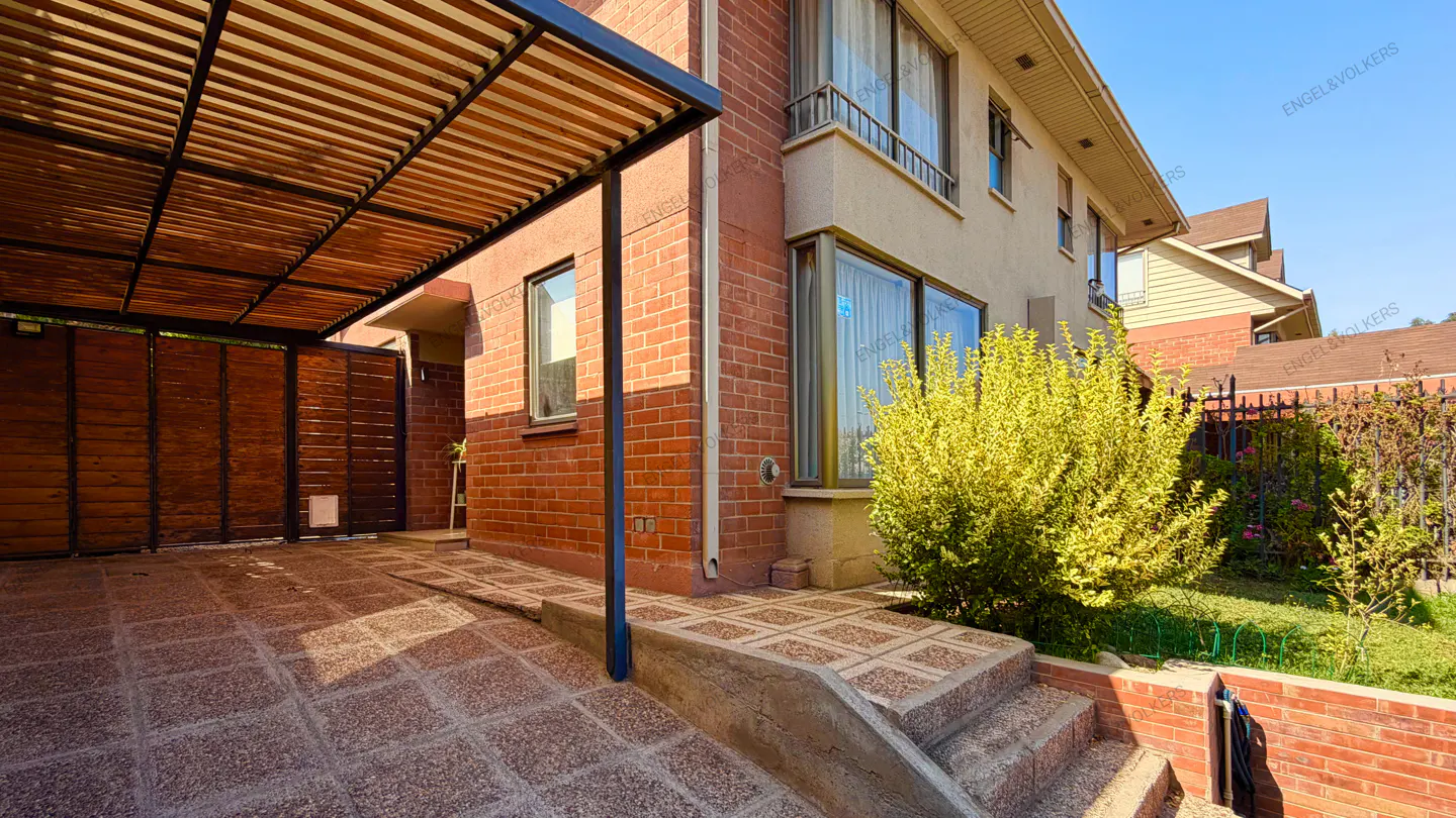 Exterior view of a two-story house with a brick facade, a wooden carport, and a green bush.