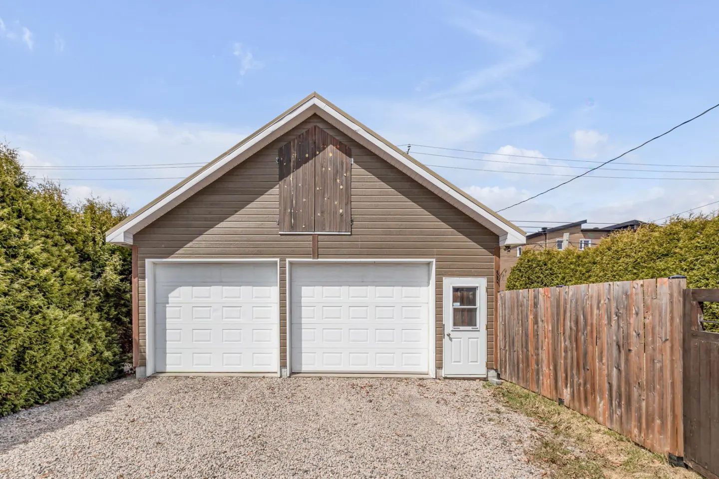 A brown garage with two white doors and a white side door, under a blue sky.