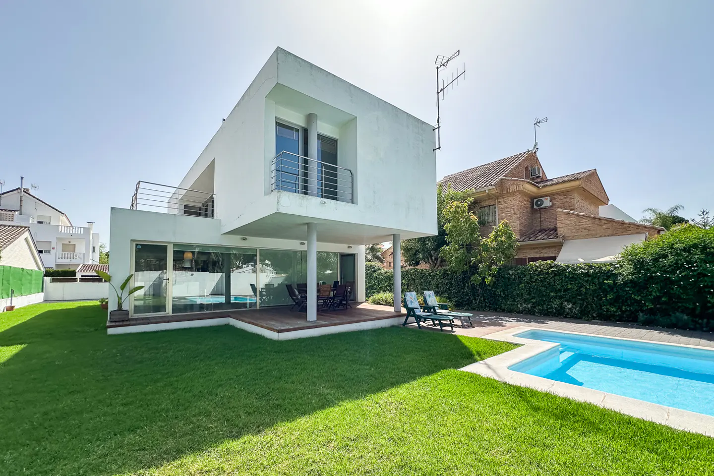 Modern white two-story house with a backyard, swimming pool, green lawn, and a covered patio area with outdoor furniture.