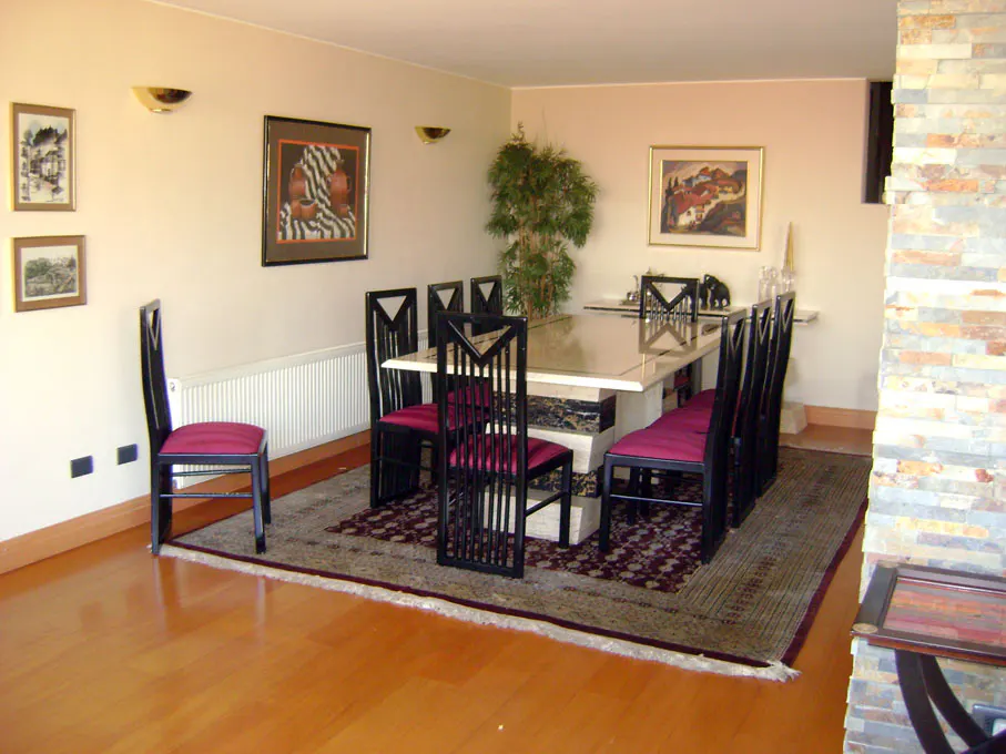 A dining room with a marble table, black chairs with red cushions, and wood floors.