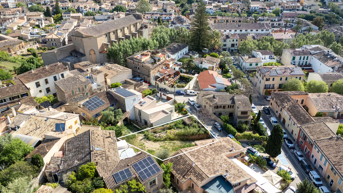 Aerial view of a vacant lot outlined in white, surrounded by buildings with terracotta roofs in a dense European town.