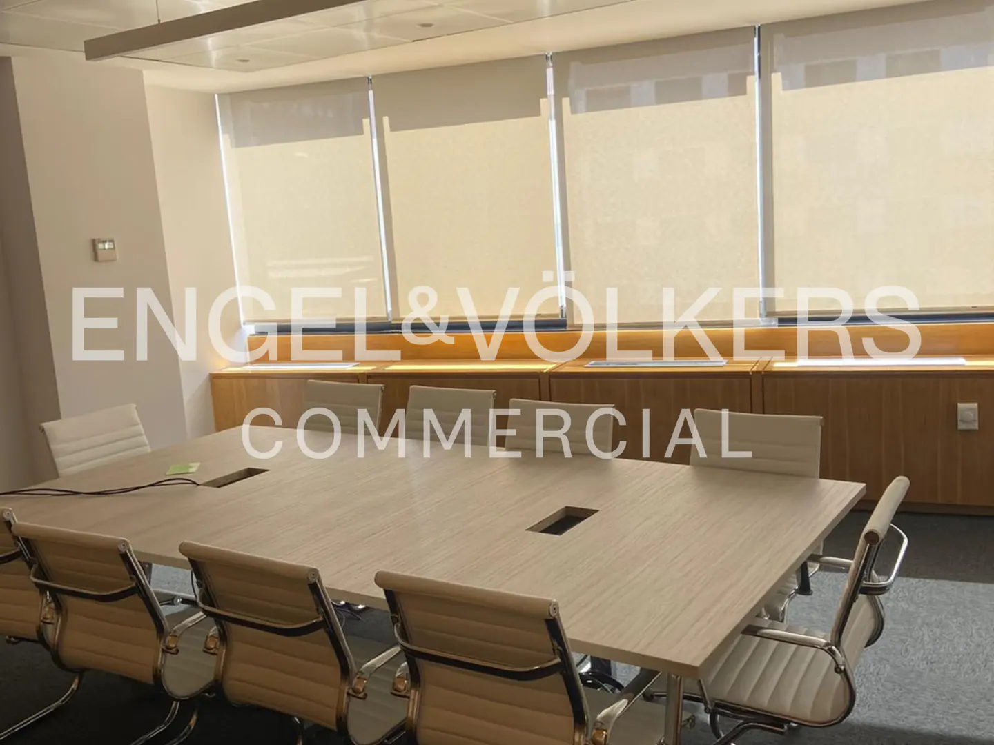 Conference room with a long light wood table, tan leather chairs, and beige window shades.