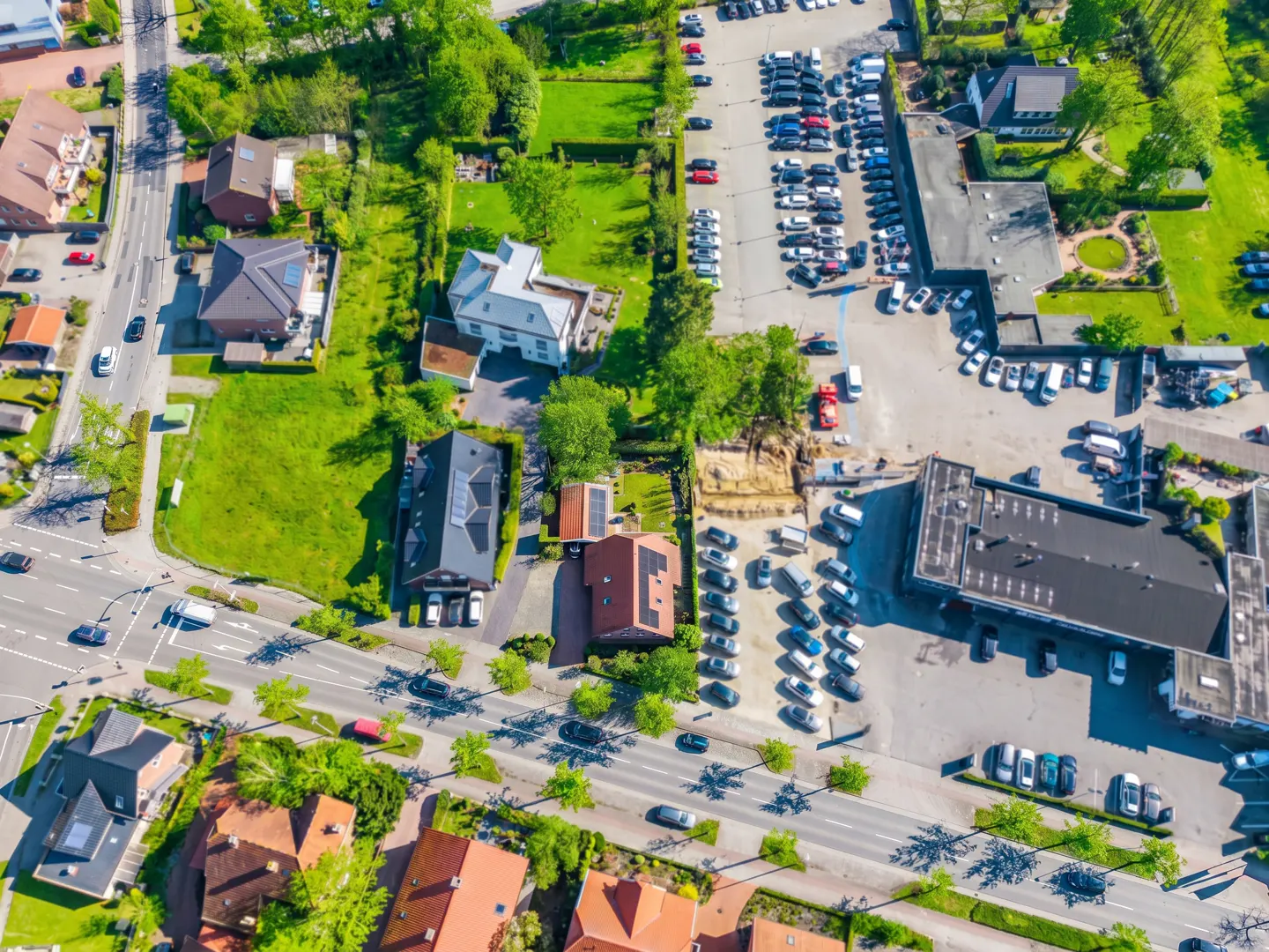 Aerial view of a neighborhood with houses, green lawns, trees, roads with cars, and parking lots.