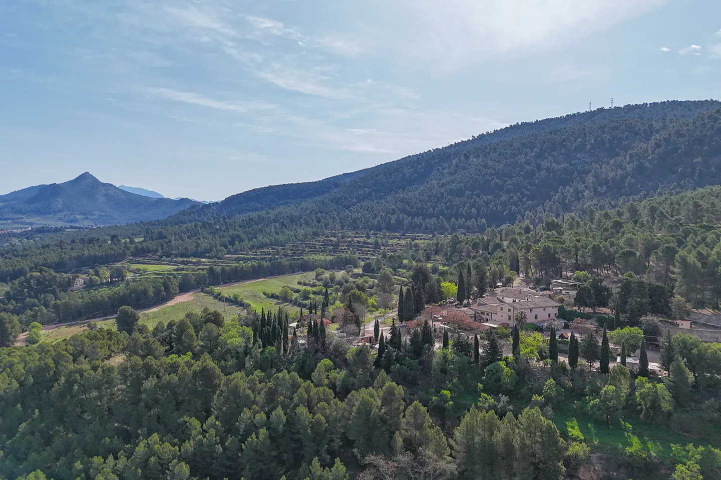 Aerial view of a property nestled in a lush, green valley with mountains in the background under a blue sky.