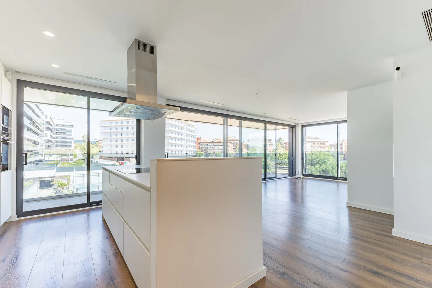 Bright, modern apartment with wood floors, white walls, and a kitchen island. Large windows offer city views.
