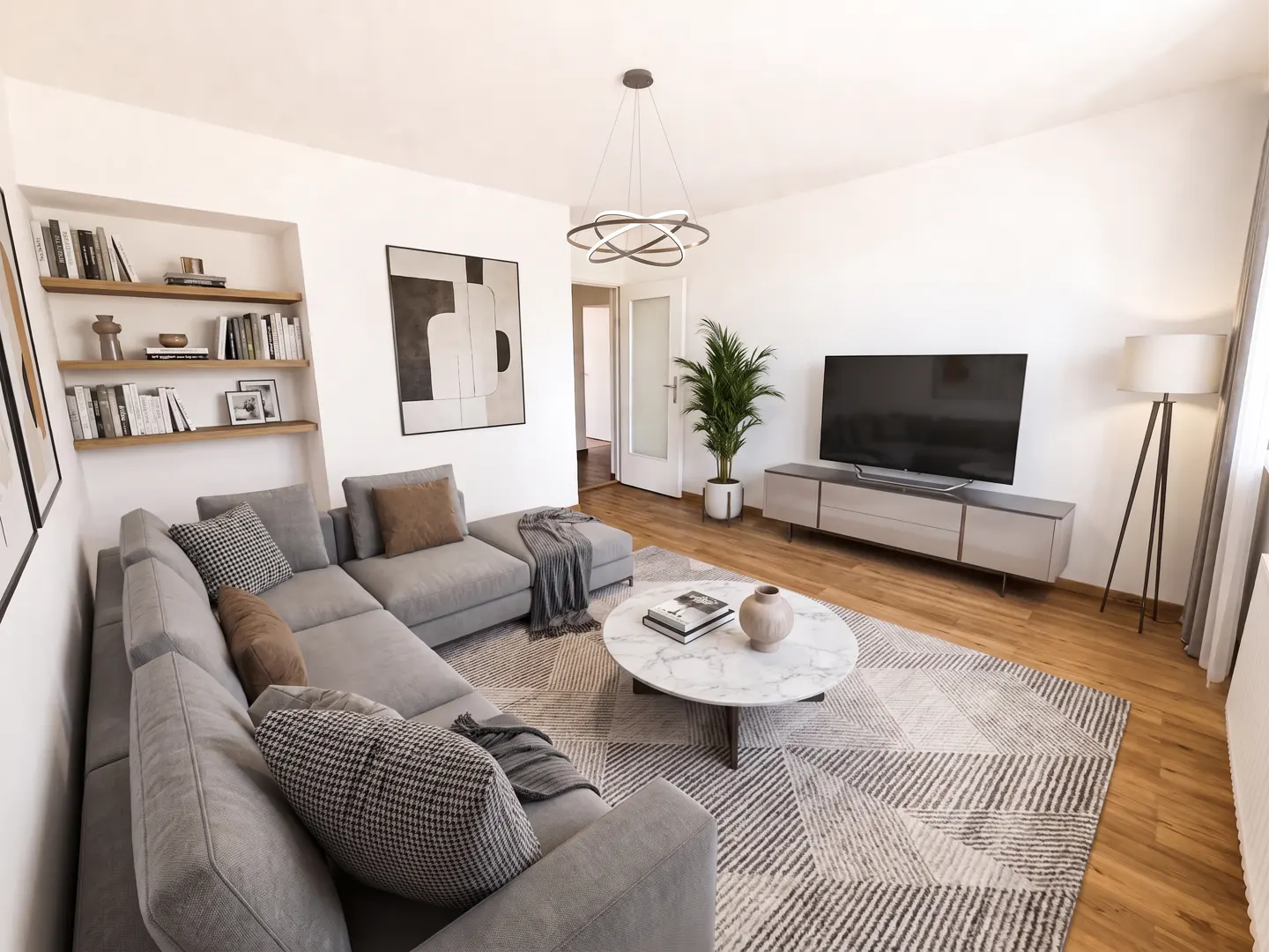 A bright living room with a gray sectional sofa, marble coffee table, and a large TV. Bookshelves and abstract art adorn the walls.