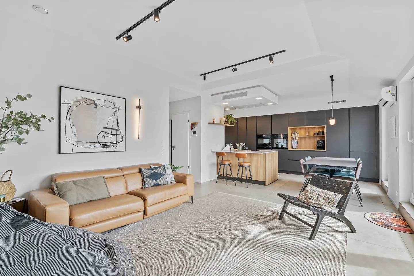 Open-concept living space with a tan leather sofa, abstract art, and a kitchen island with bar stools.