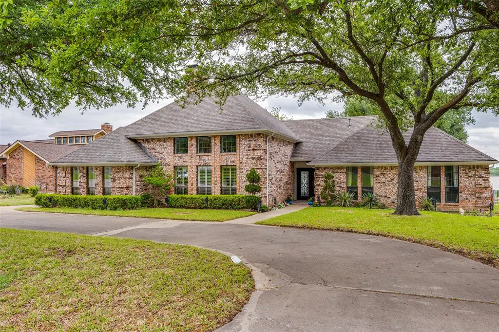 A large, single-story brick house with a gray roof and a curved driveway. Green trees frame the house.