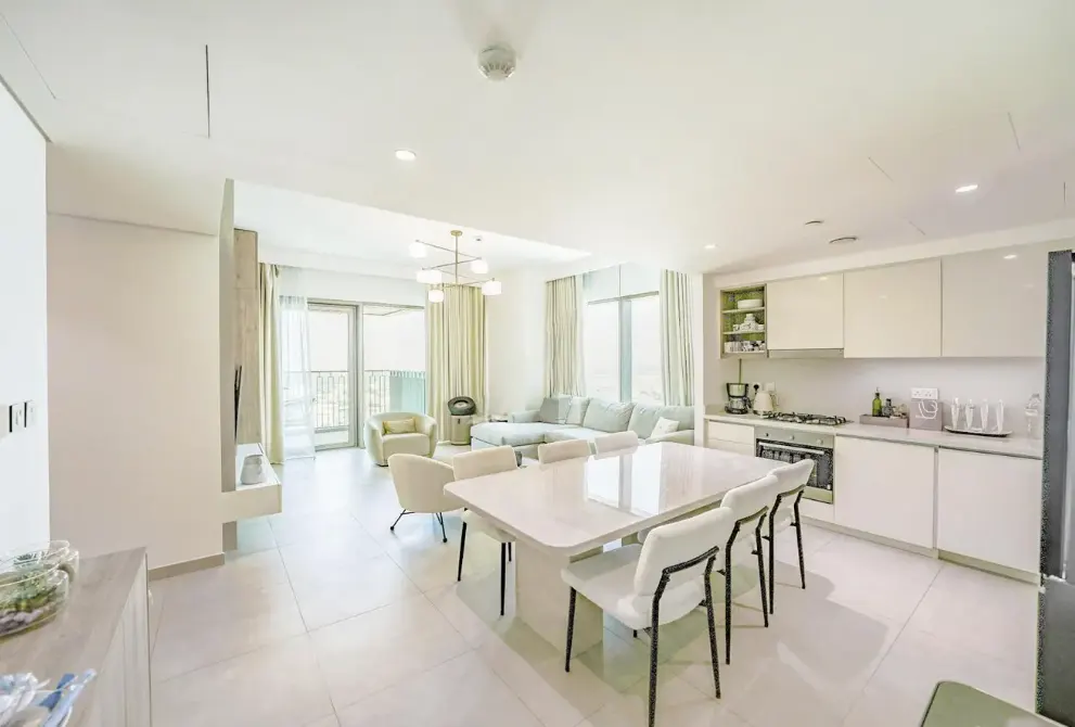 Modern open-plan apartment with a white dining set, sleek kitchen, and a bright living area with balcony access.