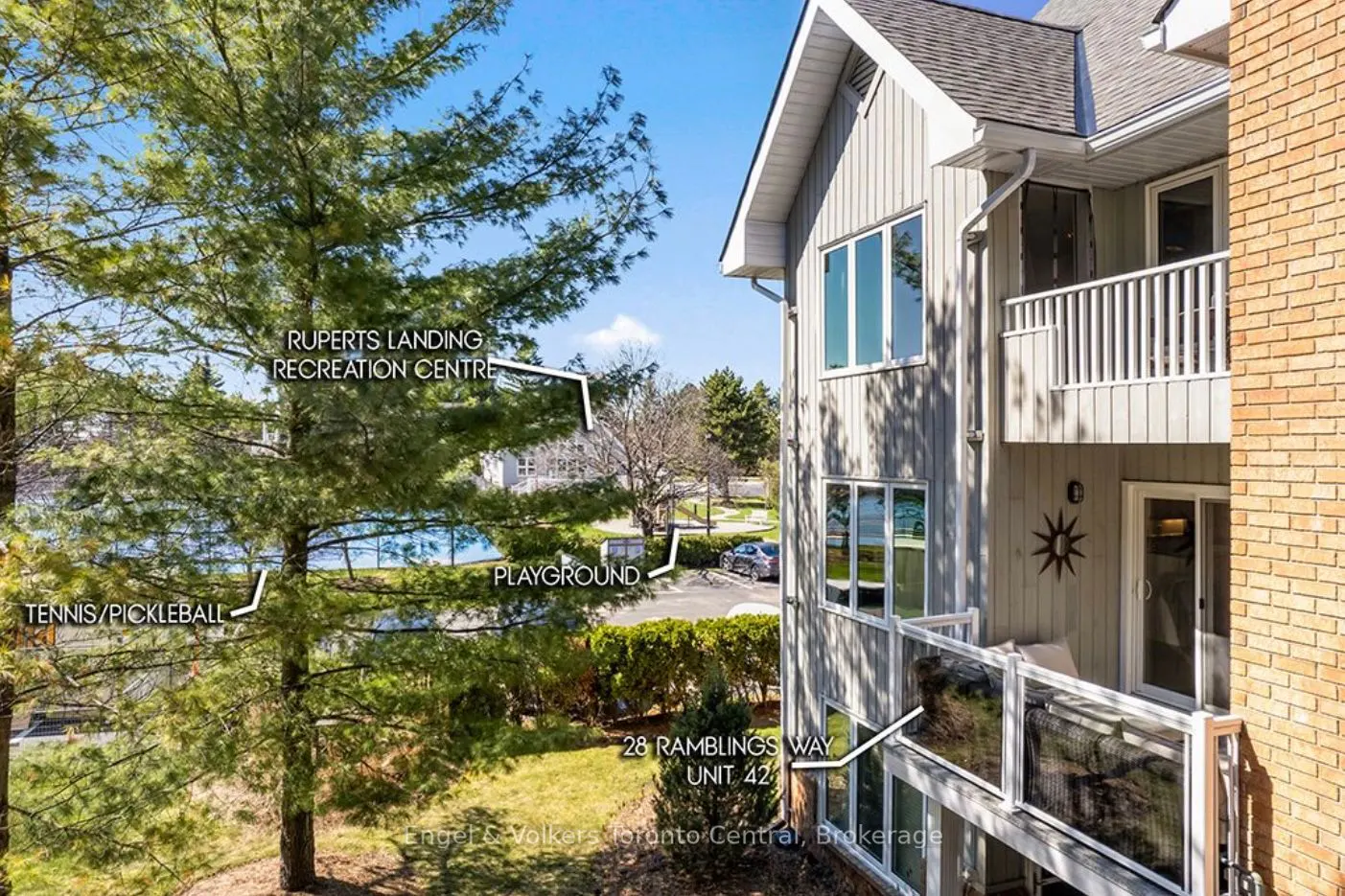 Exterior view of a condo at 28 Ramblings Way, Unit 42, with a balcony, gray siding, and brick accents. Recreation center visible.