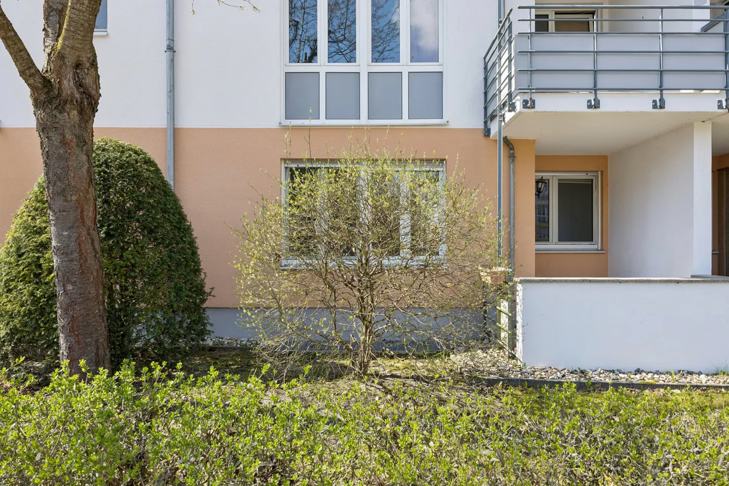 Exterior view of a two-story building with peach and white siding, a balcony, and green bushes in front.