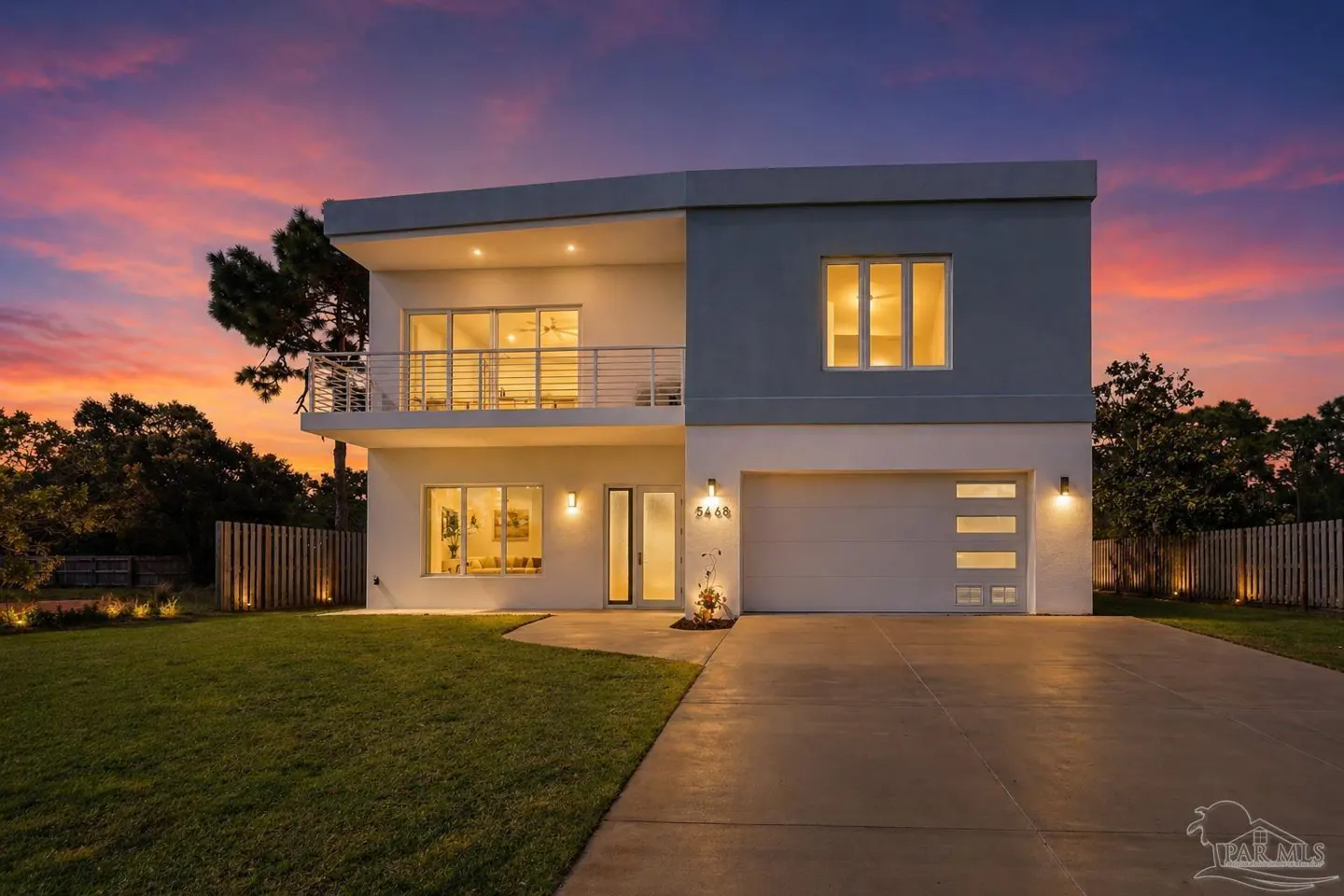Two-story modern home with a balcony, white and gray exterior, and a two-car garage at dusk.