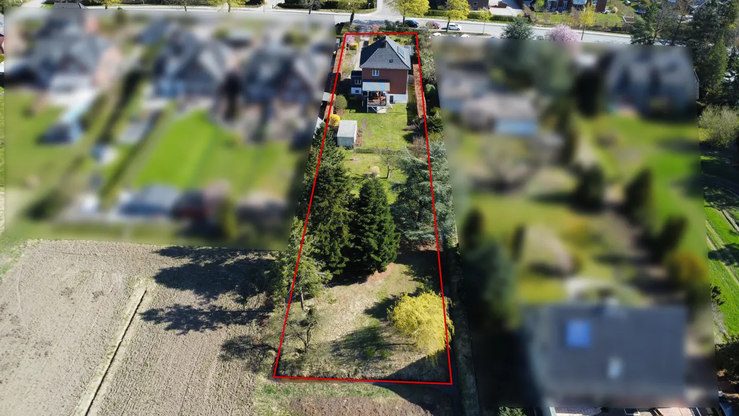 Aerial view of a property outlined in red, featuring a house, lawn, trees, and a field in the foreground.