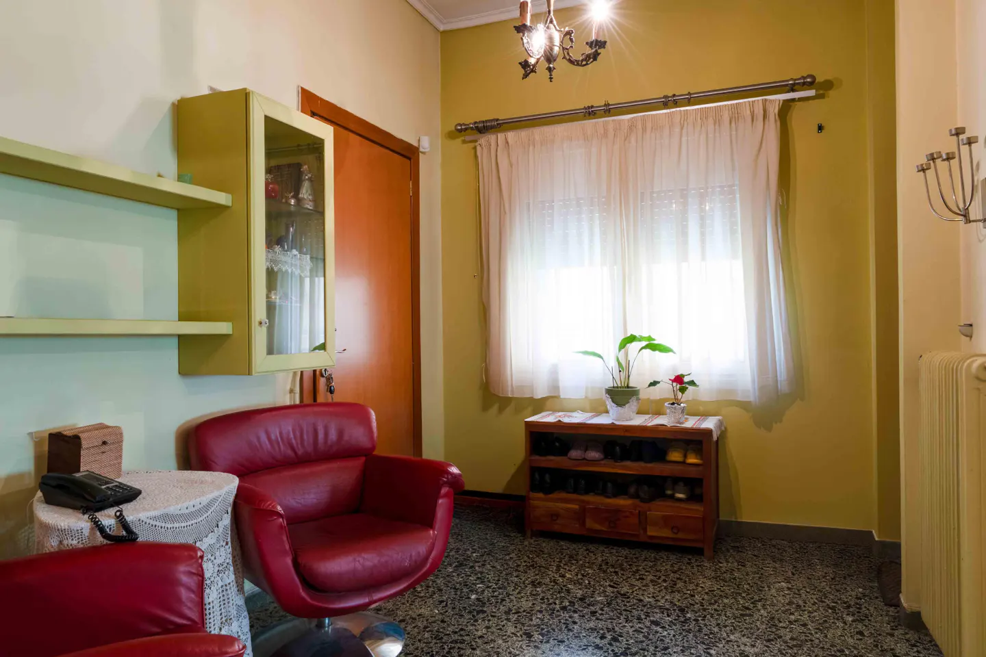 A cozy living room with red leather chairs, a wooden shoe rack, and a bright window.